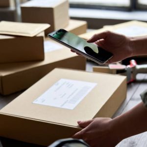 Female warehouse worker seller, small stock business owner holding phone scanning retail package parcel bar code on commercial shipping box delivery order on smartphone using mobile app.