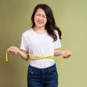 Young Asian girl holding a tape measure annoyed by weight gain